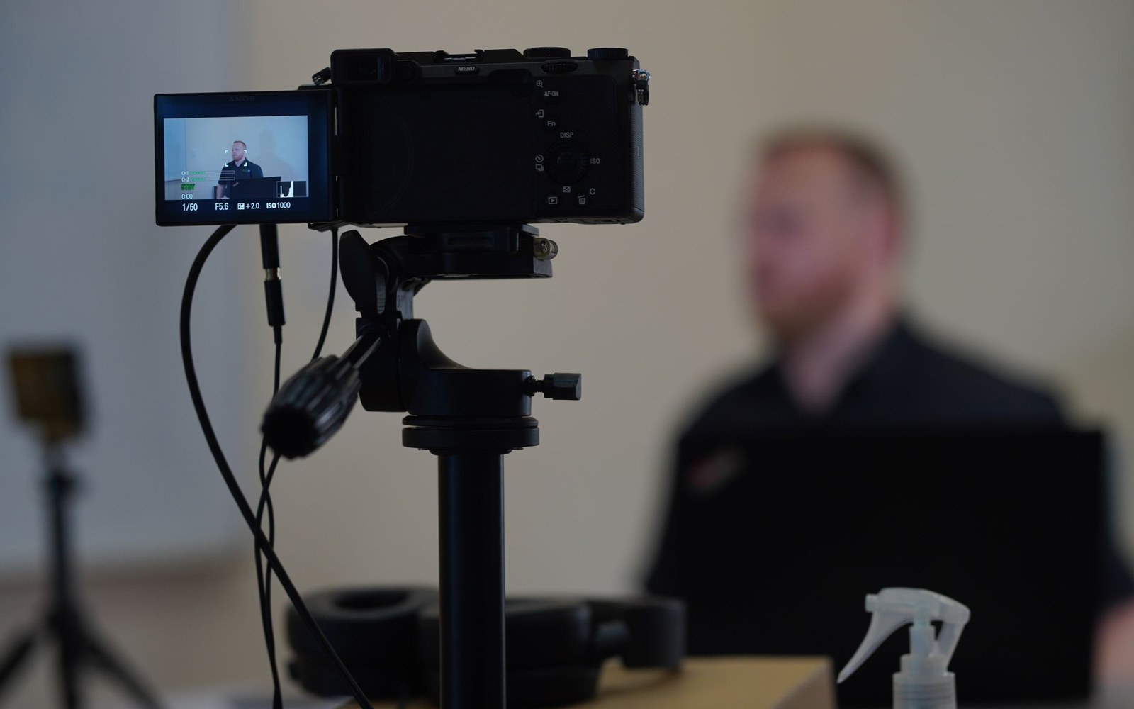 A camera on a tripod films a seated man, with his image visible on its flip screen
