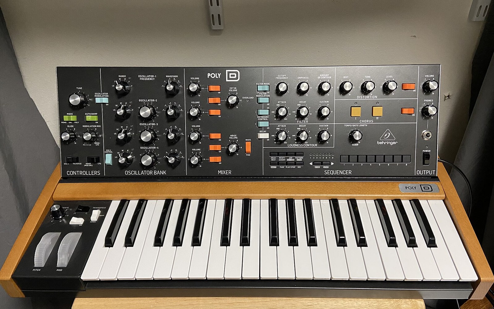 Behringer Poly D synthesizer with knob-laden control panel above a wooden-cased keyboard