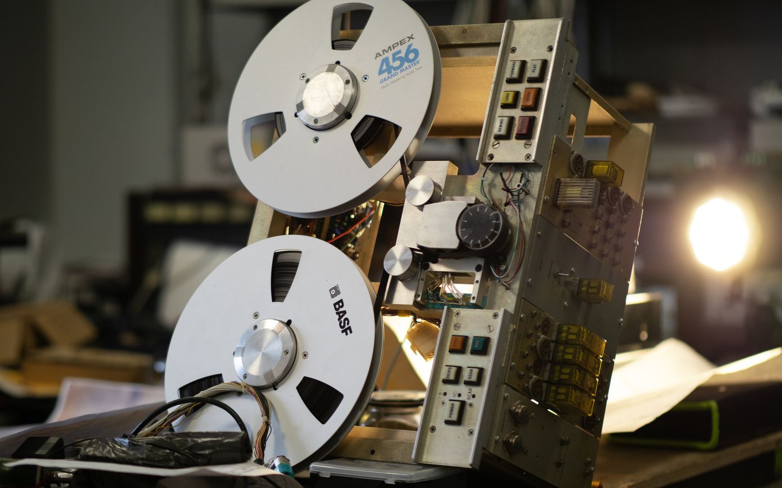 Open reel-to-reel tape machine with exposed circuit boards and control buttons on a workbench