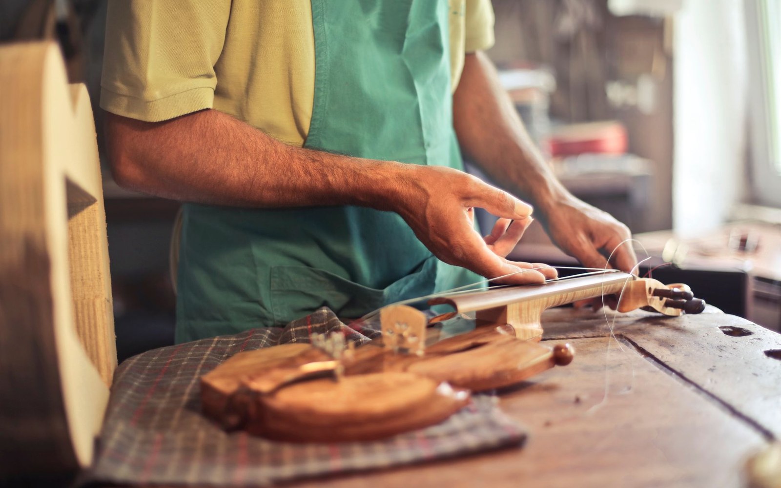 Craftsman restringing a violin bow at a wooden workbench in his workshop