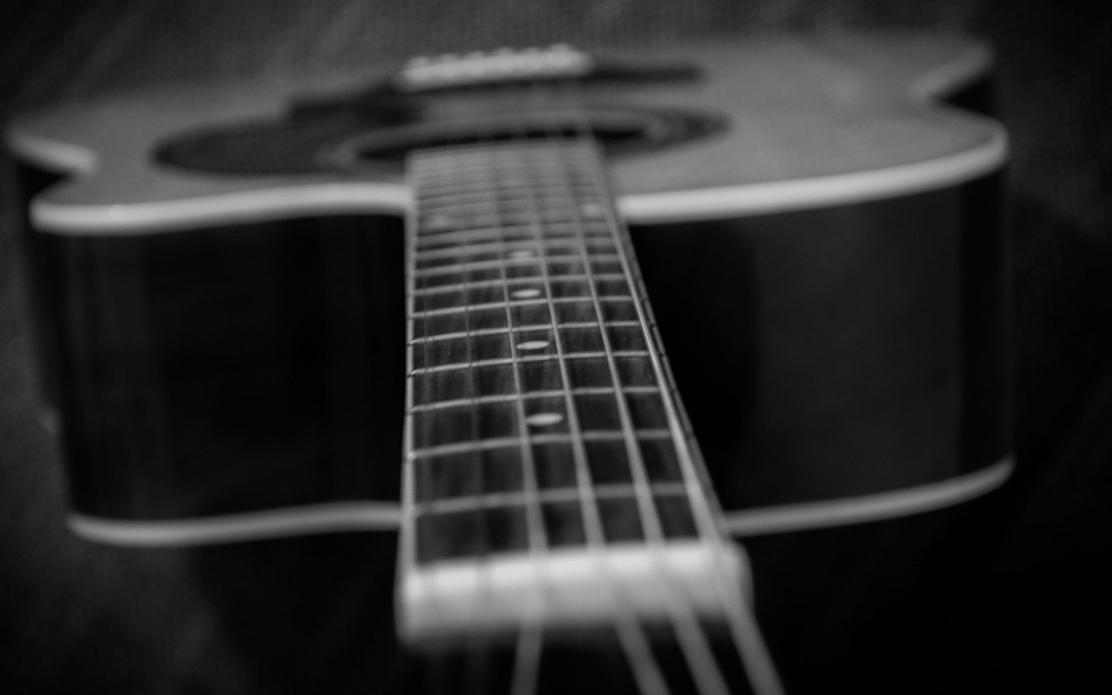 Close-up of an acoustic guitar's neck and fretboard in black and white