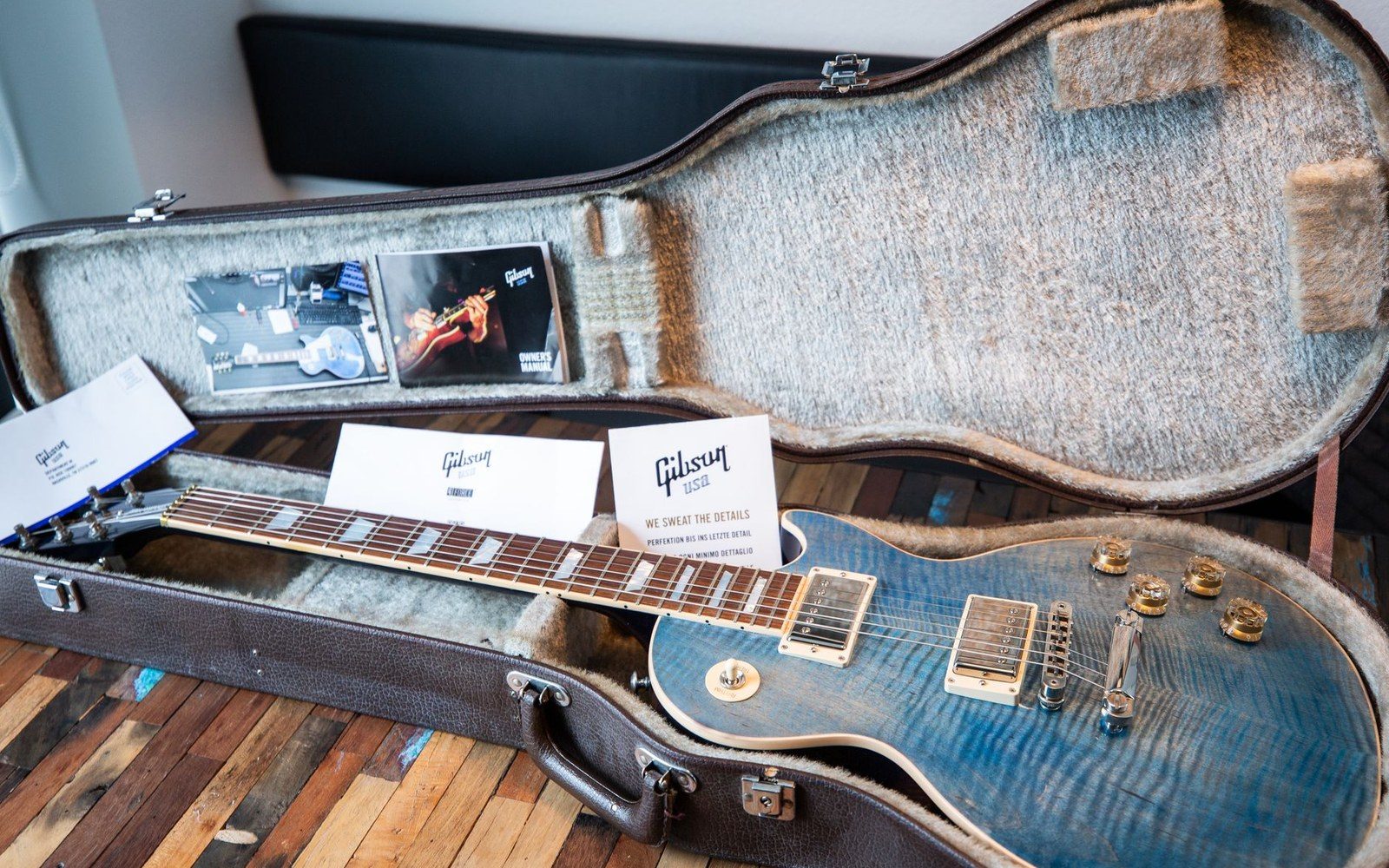 A blue flame-top Gibson Les Paul guitar resting in its open hardshell case with paperwork
