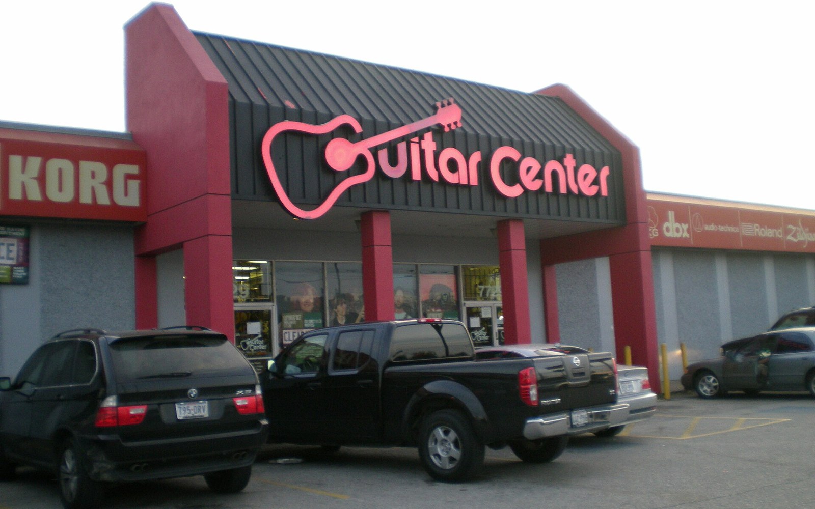 Guitar Center storefront with guitar-shaped sign, parked vehicles in front lot