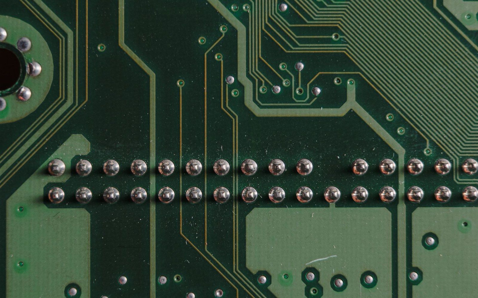 Close-up of rows of solder joints and copper traces on a green circuit board
