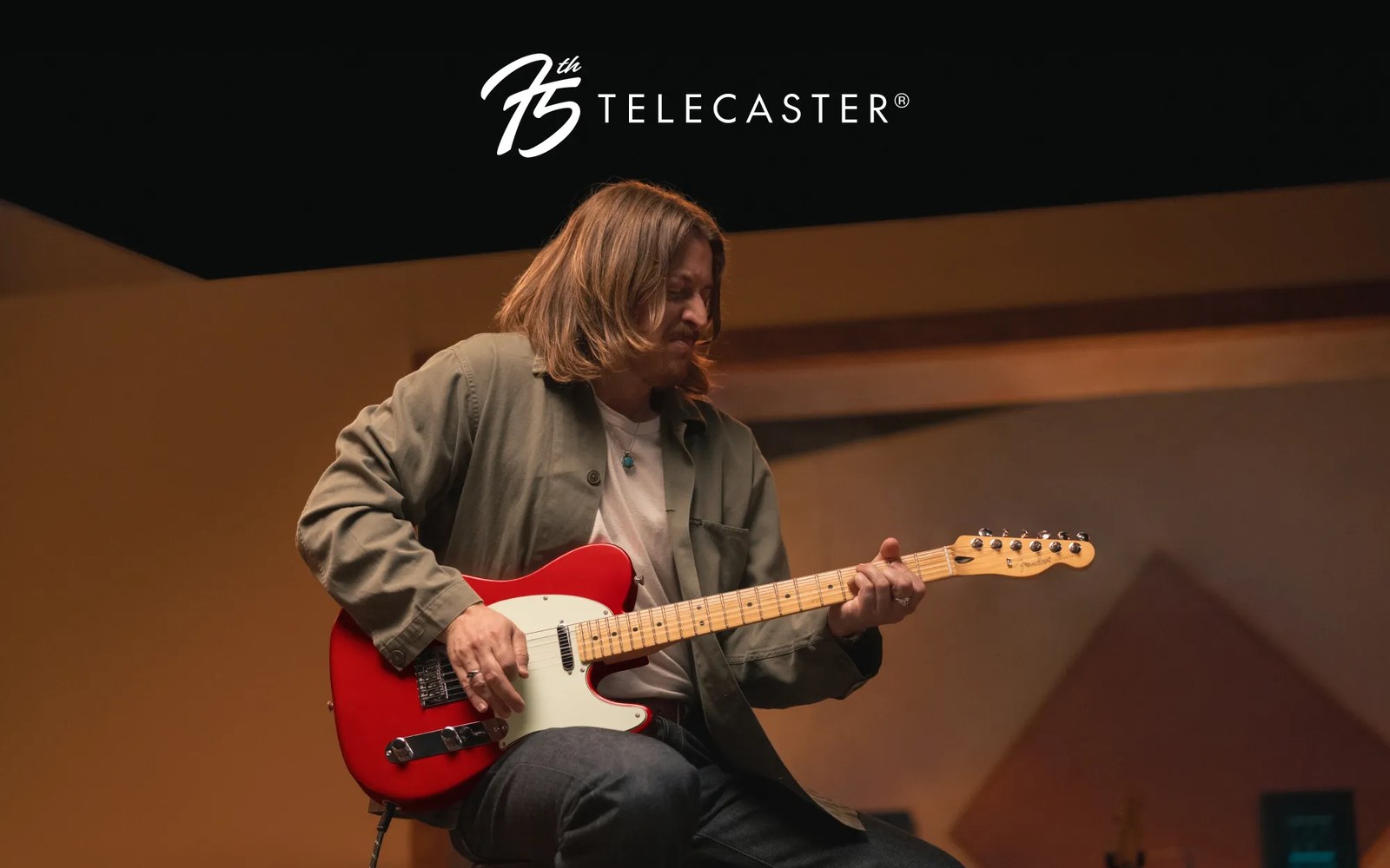 Musician sitting and playing a red Fender Telecaster guitar under a 75th anniversary logo