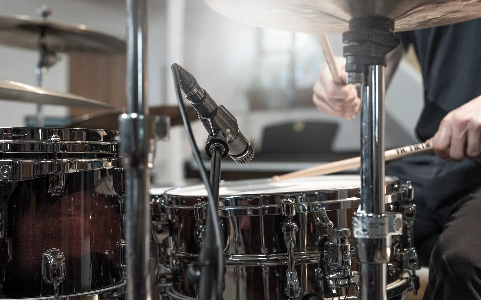 A microphone clipped near a snare drum as a drummer plays with sticks