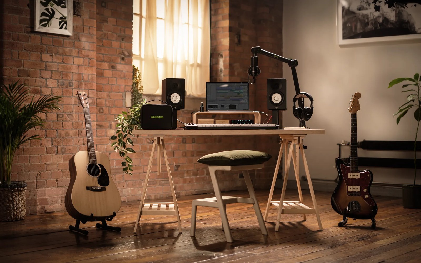 Home studio desk with monitor speakers, keyboard, boom-mounted microphone, and guitars flanking it