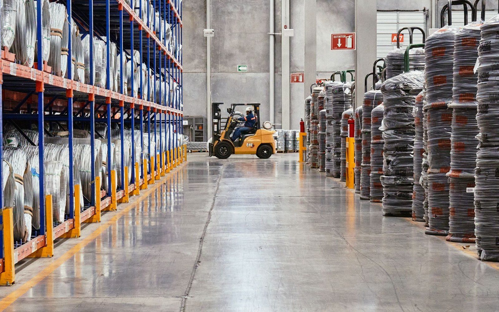 A forklift moves between tall shelves of wrapped coils in a warehouse aisle