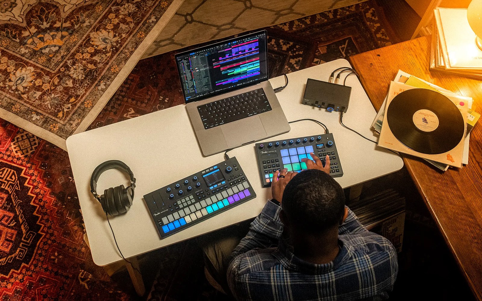 Overhead view of a producer using MIDI pad controllers and a laptop beside vinyl records