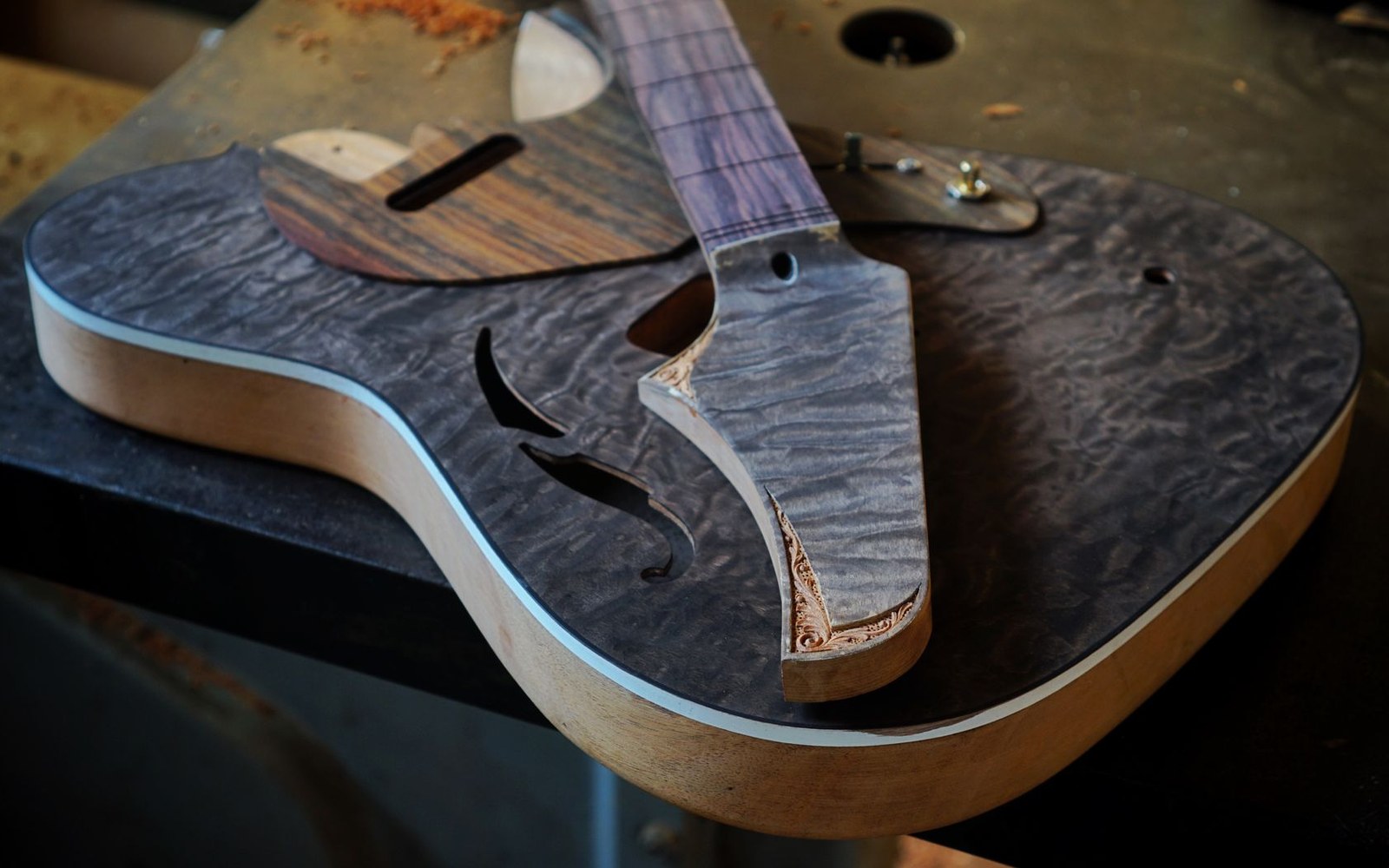 A luthier's repair bench with an acoustic guitar body open, adult hands using a palette knife near the kerfing, tools laid out in the background