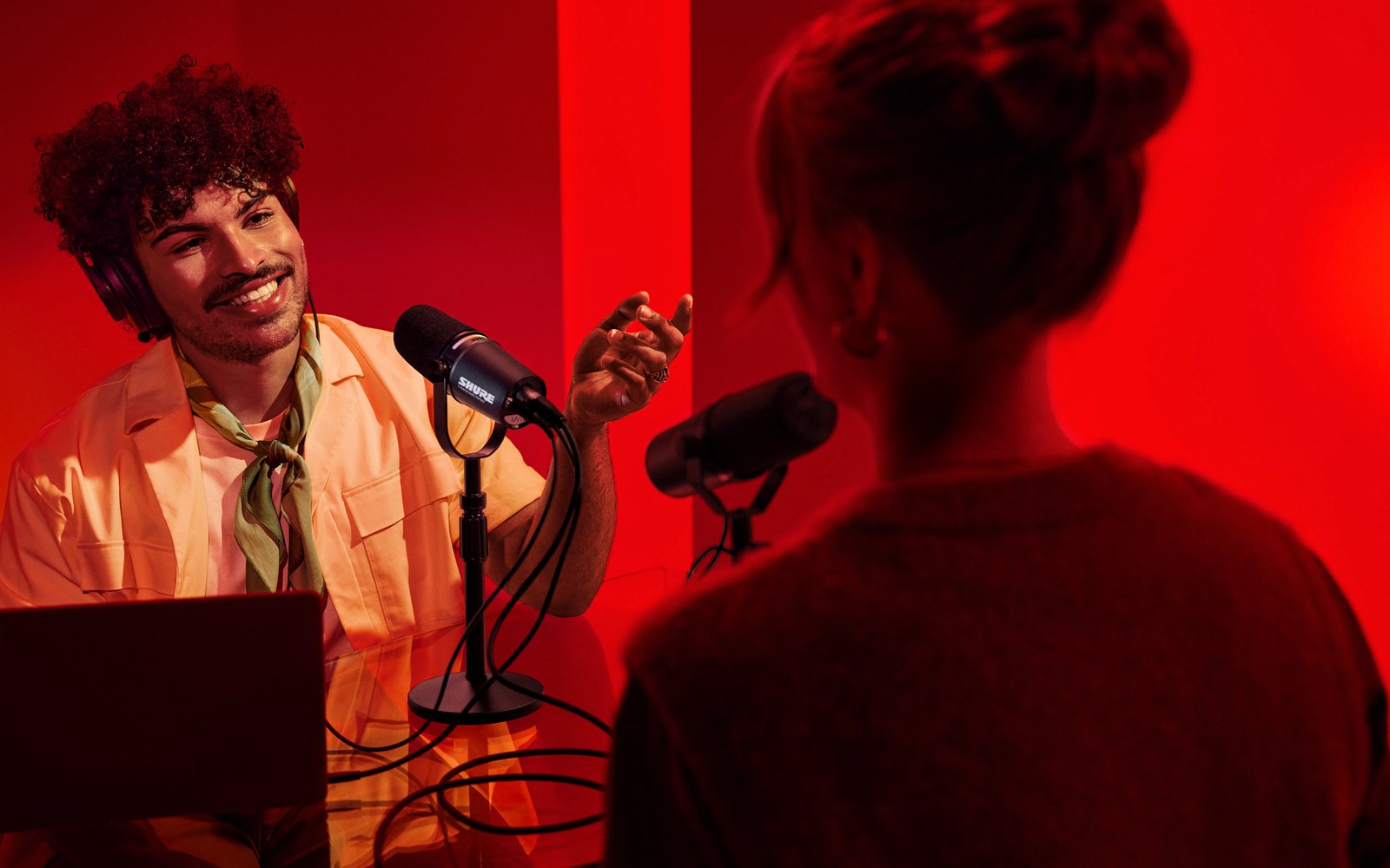 A Shure SM7B on a boom arm over a recording desk with an audio interface visible behind it, adult operator's hands adjusting the arm